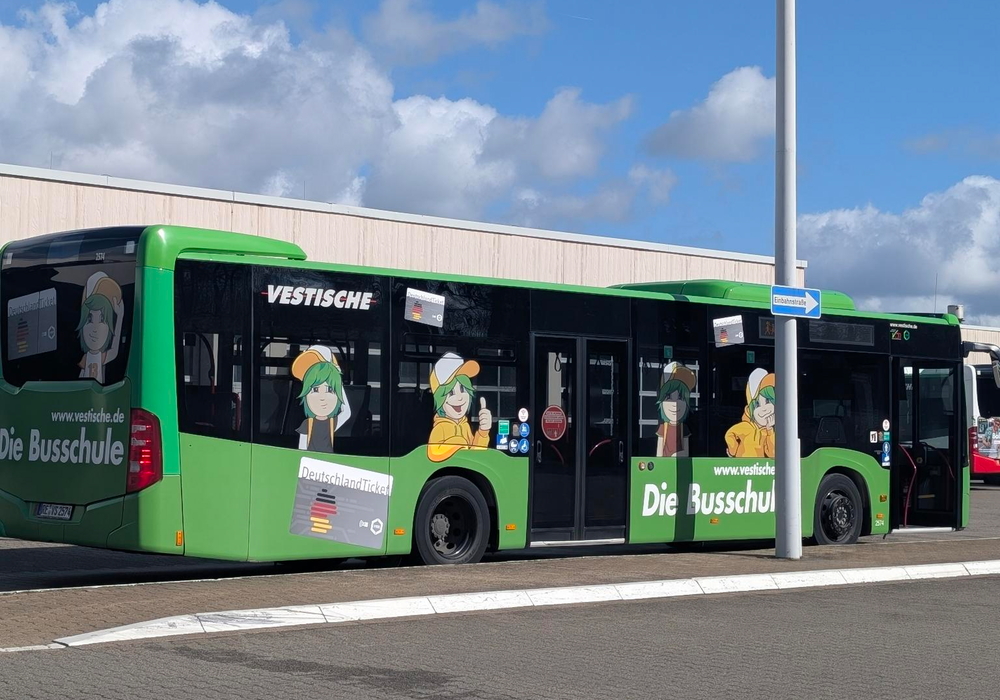 Seitliche Ansicht eines grünen Schulbusses. Im Hintergrund ist blauer Himmel zu sehen, im Vordergrund Pflastersteine.