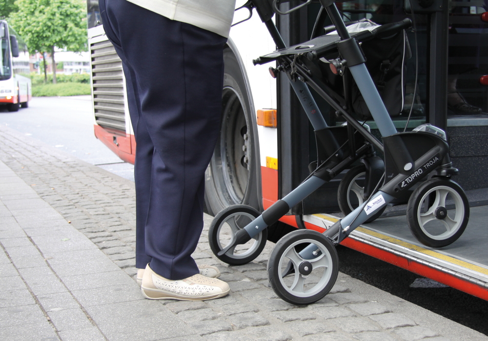 Eine Person steigt mit einem Rollator durch die hintere Tür in einen Bus ein.