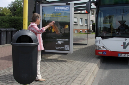 An einer Haltestelle gibt eine ältere Frau ein Handzeichen, damit der Bus anhält.