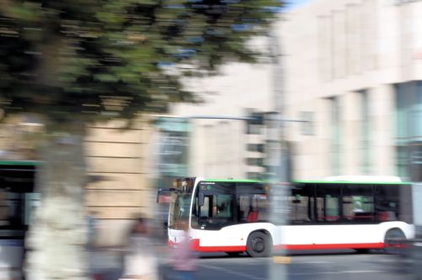 Ein Bus fährt durch die Stadt. Bäume, weitere Busse und Personen im Hintergrund sind durch die Bewegung verschwommen.